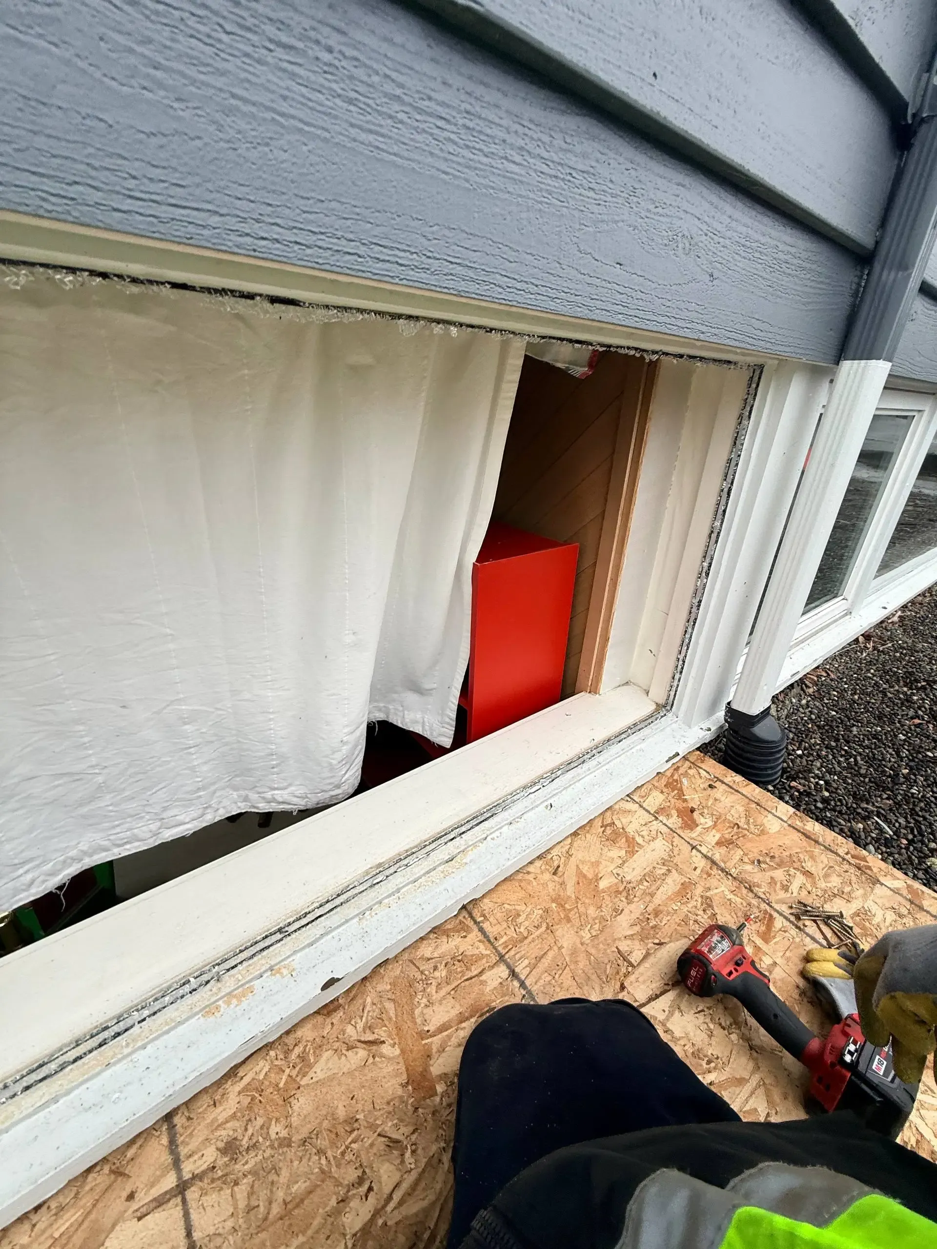 An exterior window opening without its glass, with tools below the existing white frame.