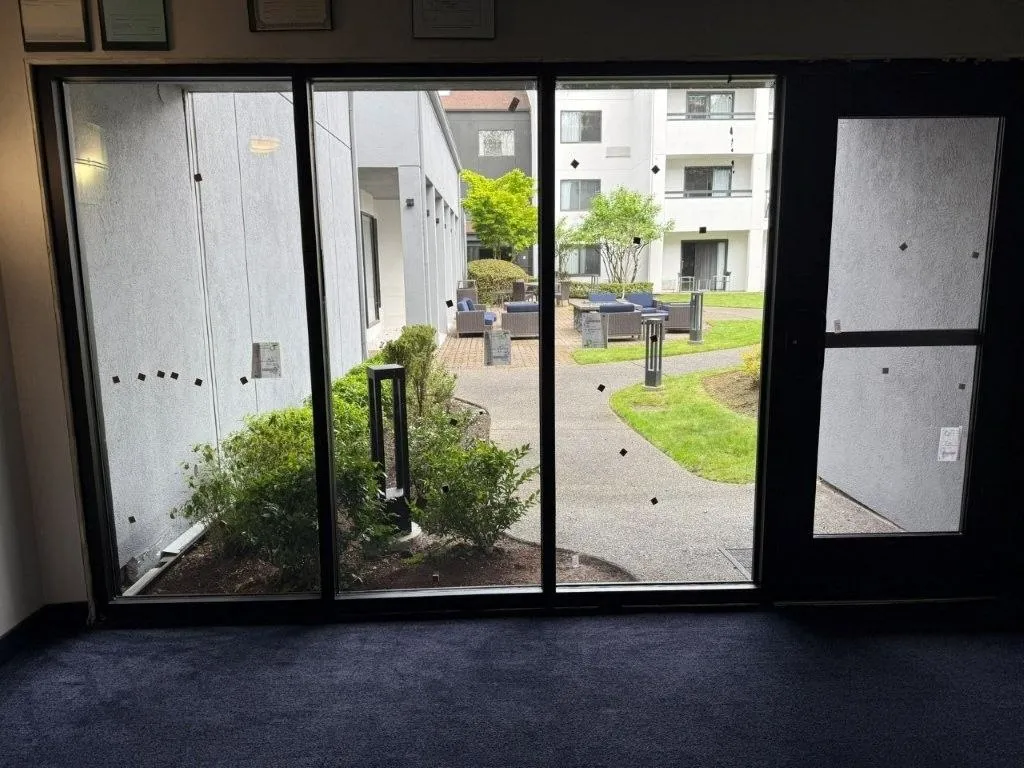 Dark-framed glass entrance looking onto a planted courtyard and neighboring windows