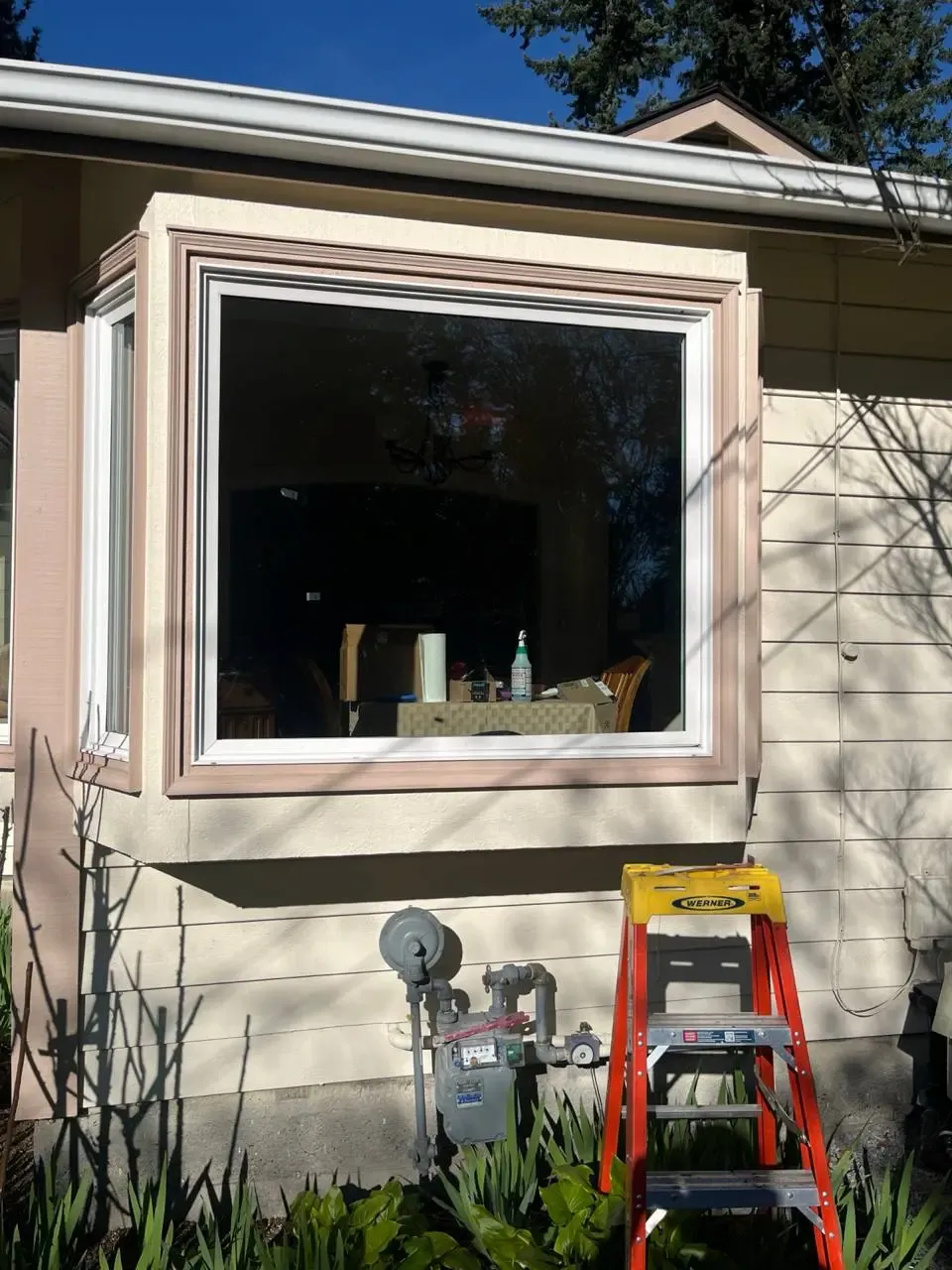 A white-framed projecting residential window, with a ladder below it.