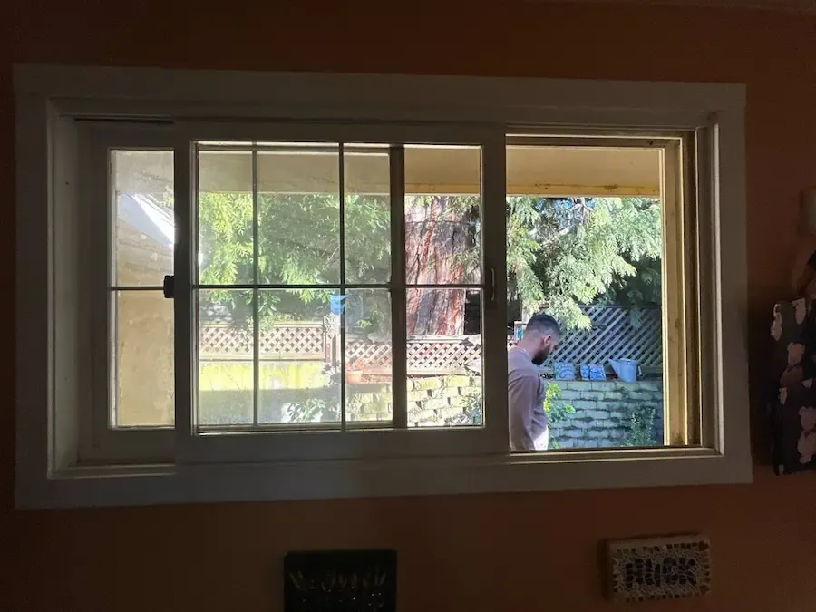Residential sliding window with divided panes and a technician working outside.