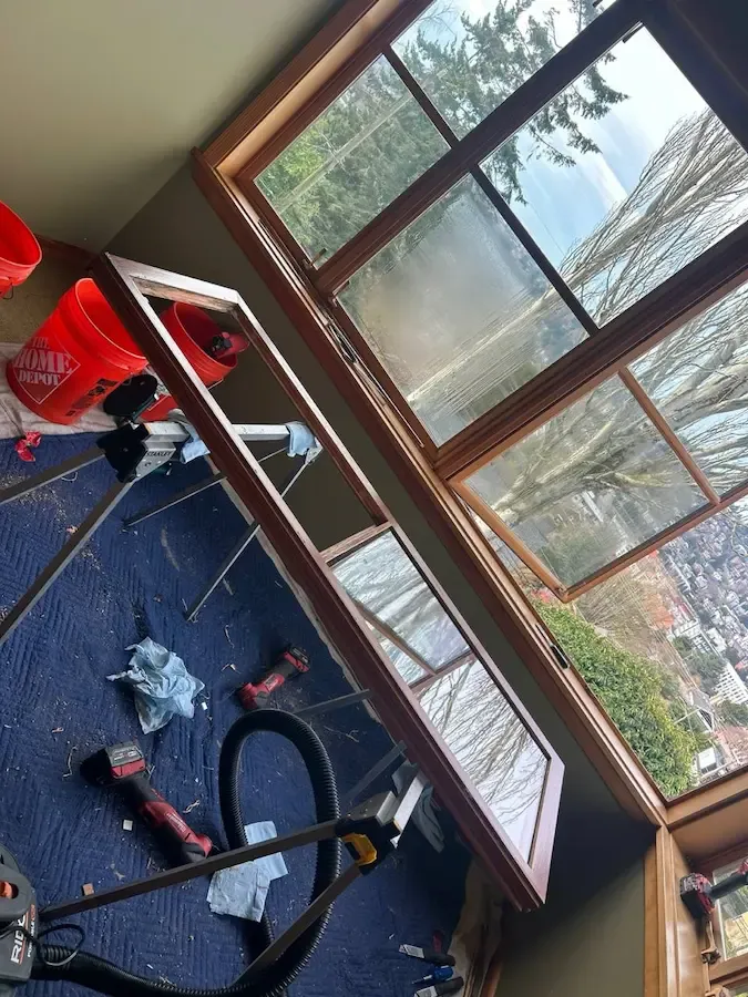 Window repair tools and a removed frame beside cloudy wood-framed window panes.