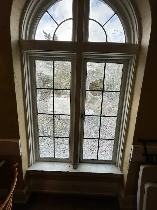 Cracked residential window glass beneath an arched transom