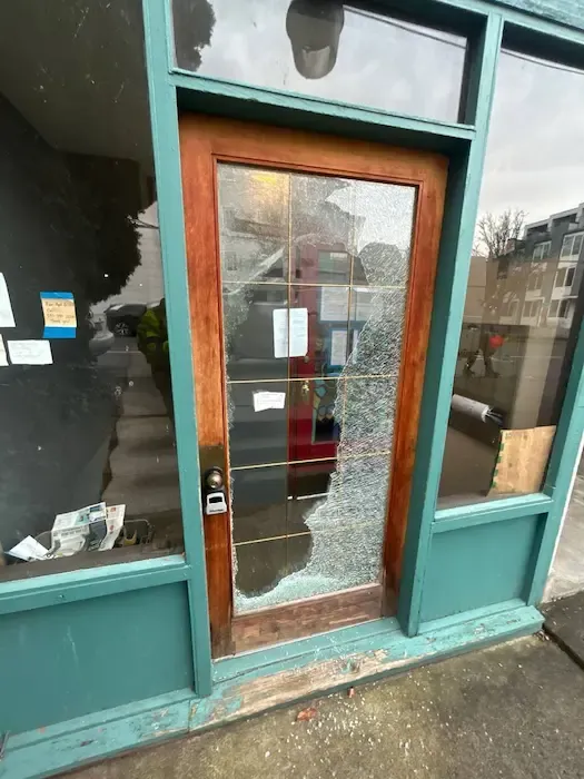 Damaged glass in a wood-framed storefront door with debris below