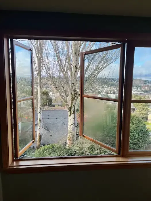 Open wood casement window with cloudiness in a lower glass pane