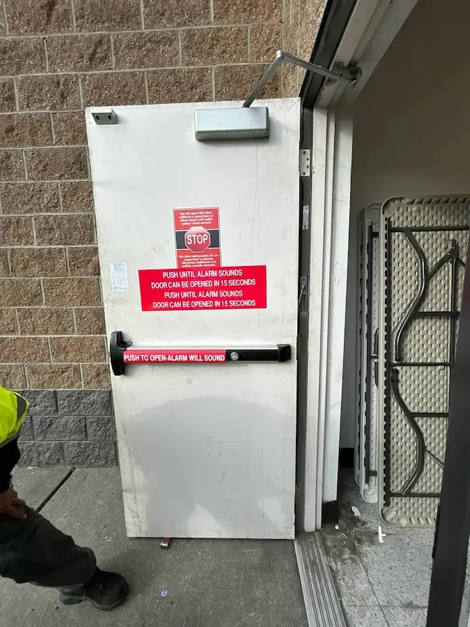 Solid white exit door with a surface-mounted closer and panic bar, shown open in its frame