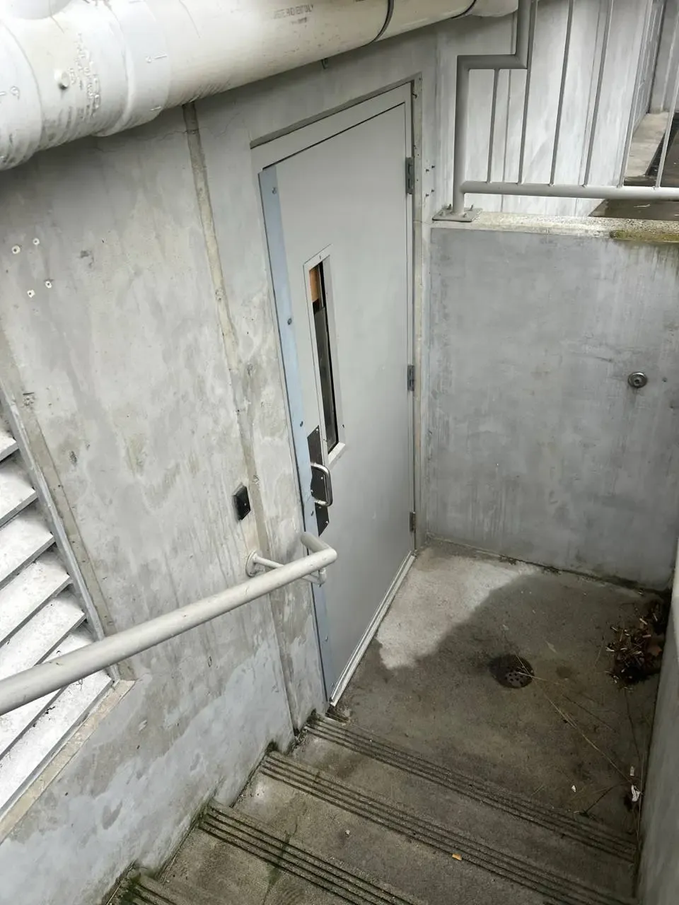 Gray service door with a narrow window at the bottom of an exterior stairwell