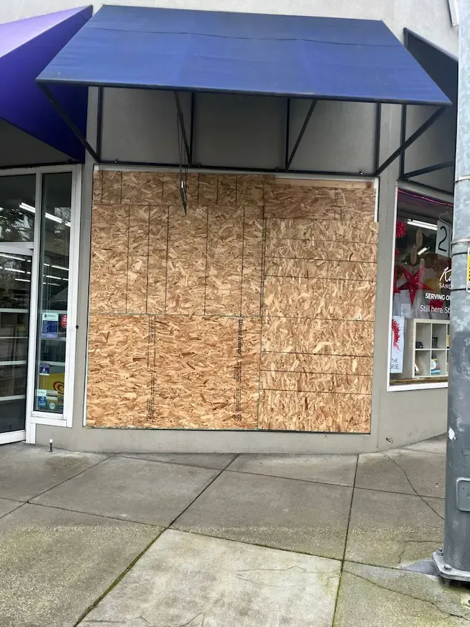 Boarded storefront display window beside a glass entrance