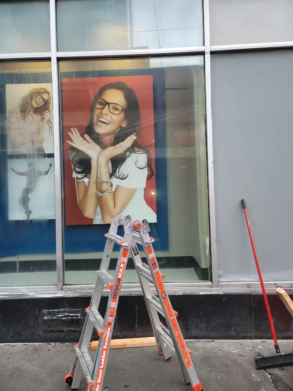 Clear glazing in the matching eyewear storefront, with a ladder and broom outside.