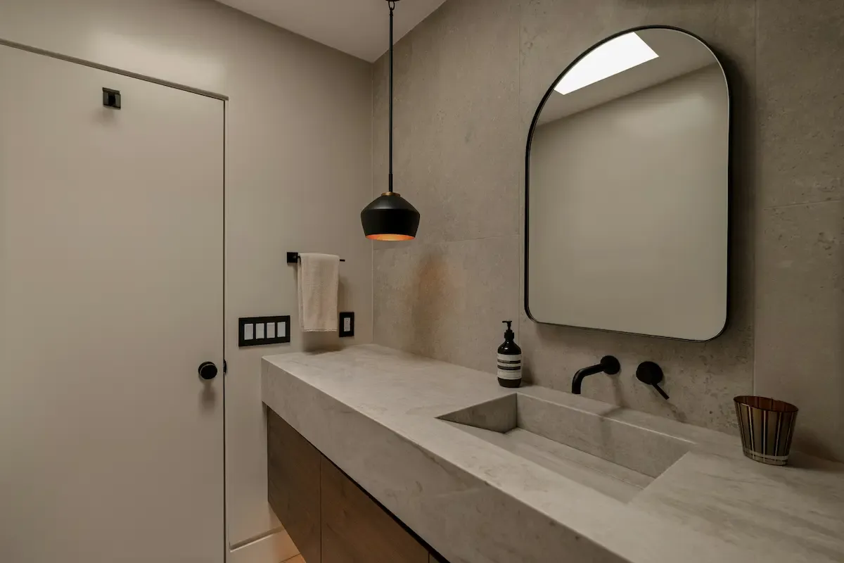 Arched wall mirror above a stone bathroom vanity with pendant lighting