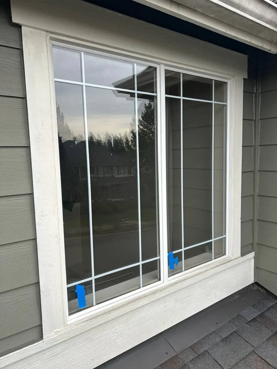 A white-framed residential window with decorative bars and blue tape near its bottom edge.