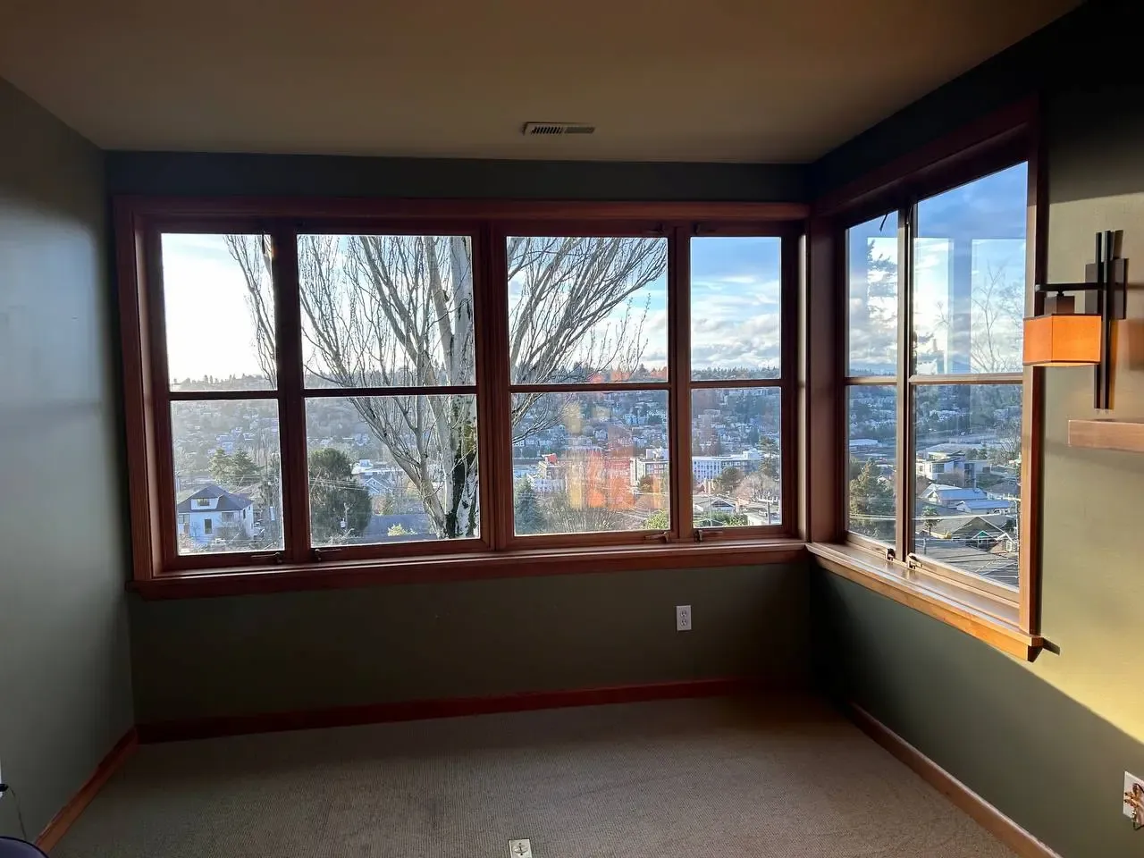 Wood-framed corner windows viewed from a room overlooking trees and houses.