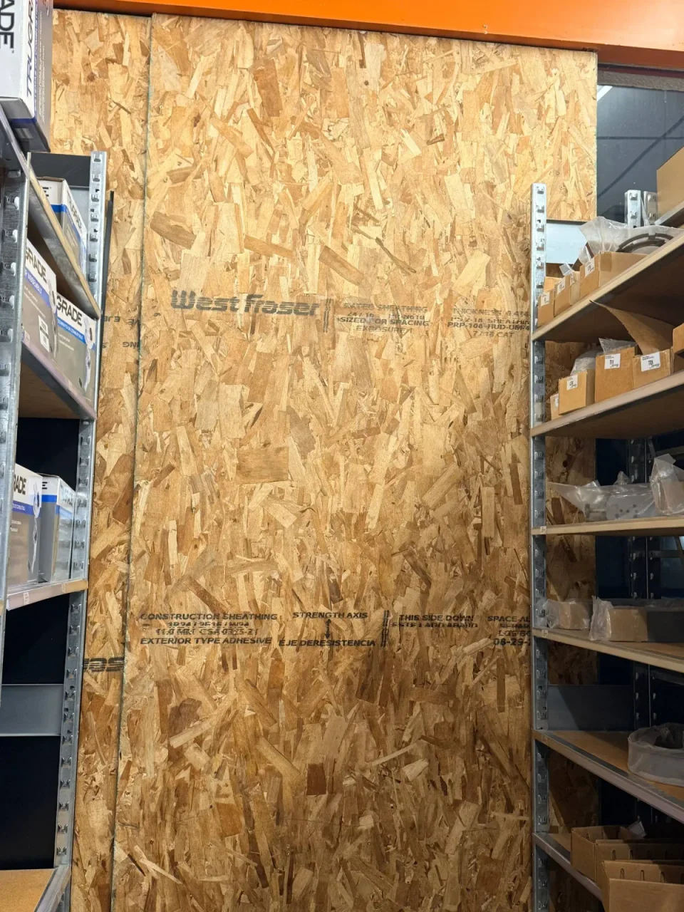 Tall timber board covering a shop opening beside shelves, photographed from inside.
