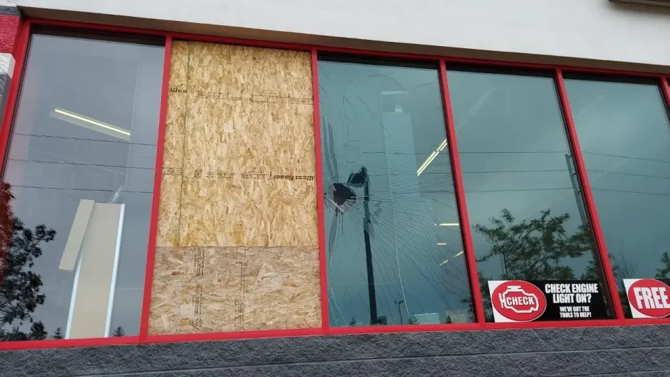 Red-framed storefront with one boarded opening beside a pane with a hole and radiating cracks.