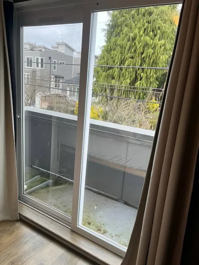 White-framed sliding glass door leading to a balcony, with curtains at the side.