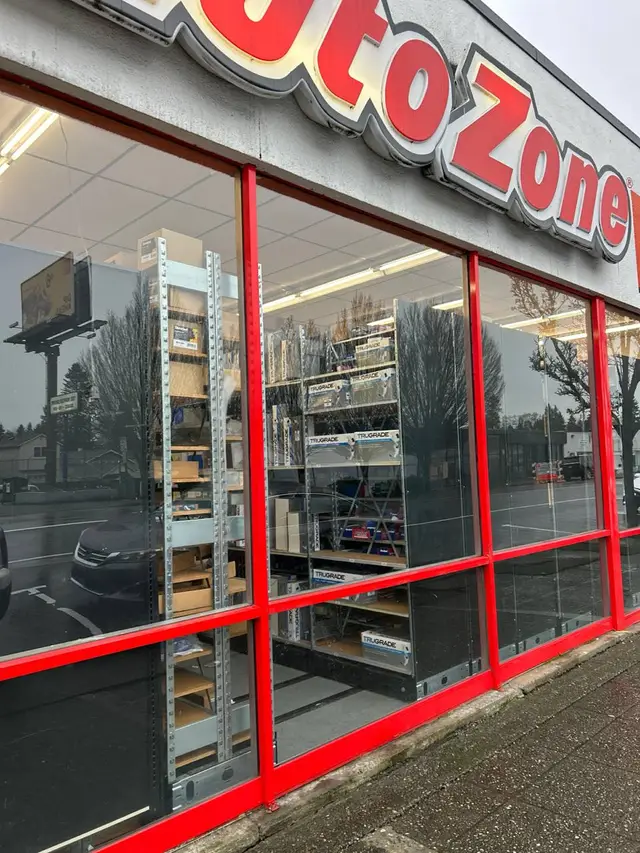 Glass panels in a red-framed storefront, reflecting the street outside.