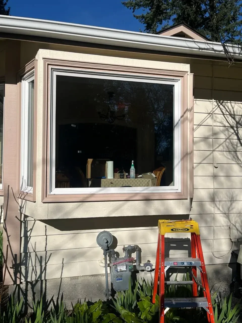 Large white-framed projecting window above a brick wall, with a ladder and equipment below.