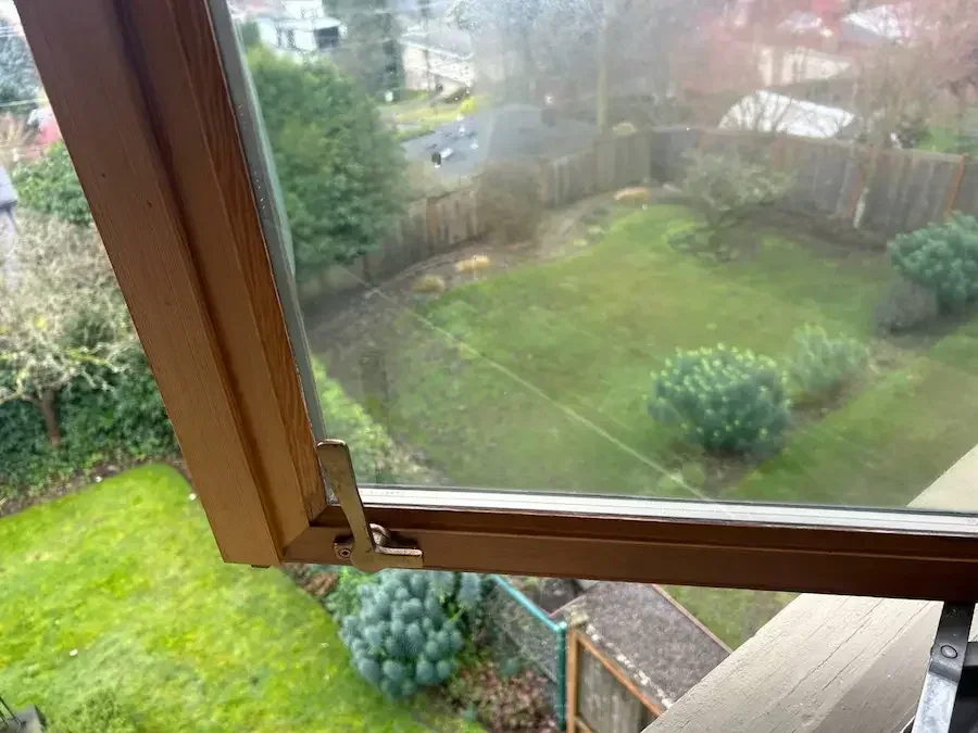 Open timber casement with cloudy marks on the glass and a garden visible beyond.