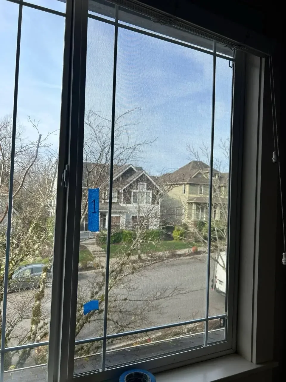 Tall dark-framed window panes with strips of blue tape and neighbouring houses visible through the glass.